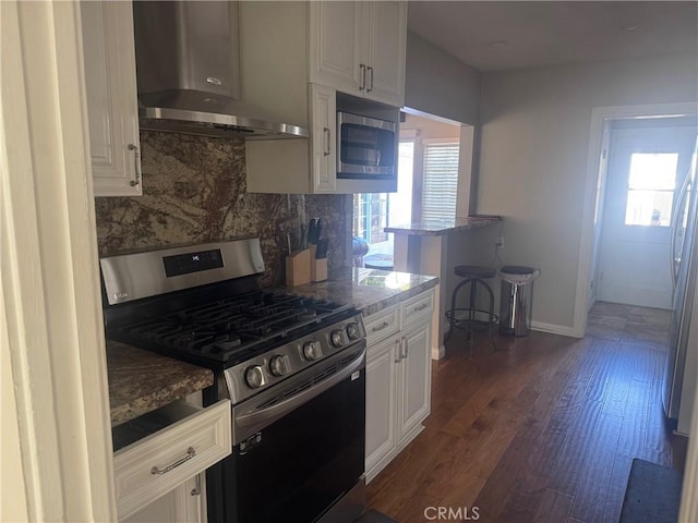 kitchen featuring white cabinetry, wall chimney range hood, stainless steel appliances, a healthy amount of sunlight, and decorative backsplash