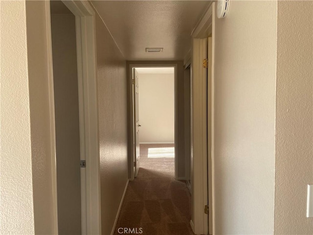 hallway featuring a textured ceiling and dark colored carpet