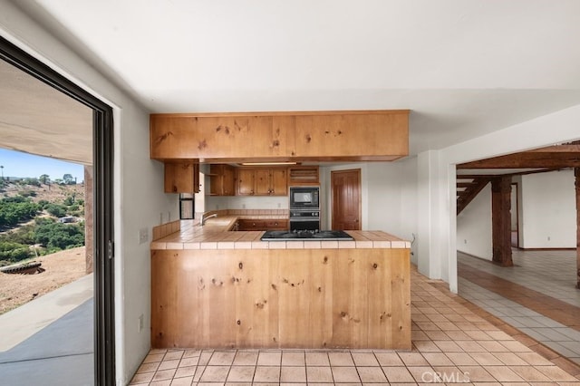 kitchen featuring black appliances, tile counters, light tile patterned floors, sink, and kitchen peninsula