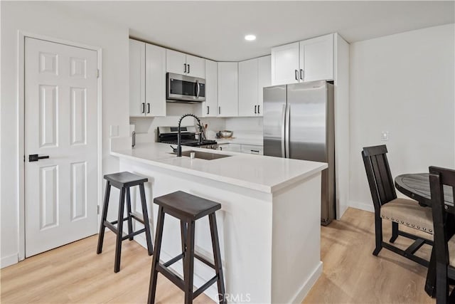 kitchen with white cabinetry, stainless steel appliances, sink, kitchen peninsula, and light hardwood / wood-style flooring