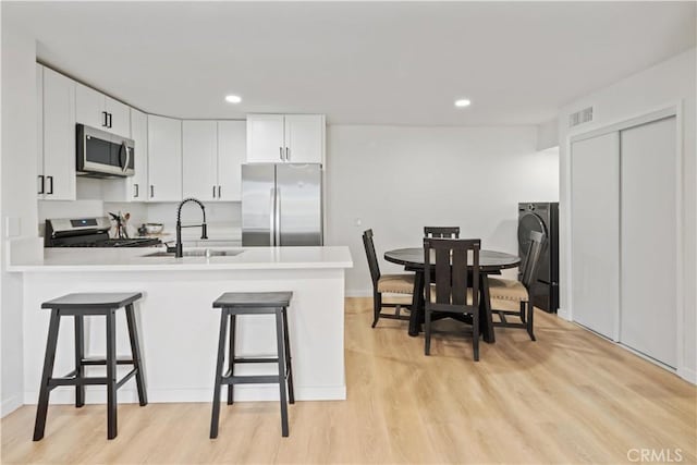 kitchen featuring kitchen peninsula, a breakfast bar area, appliances with stainless steel finishes, white cabinets, and sink