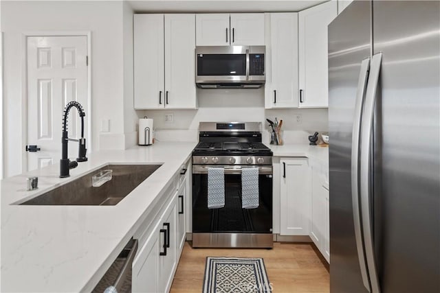 kitchen featuring sink, white cabinetry, light hardwood / wood-style flooring, appliances with stainless steel finishes, and light stone counters