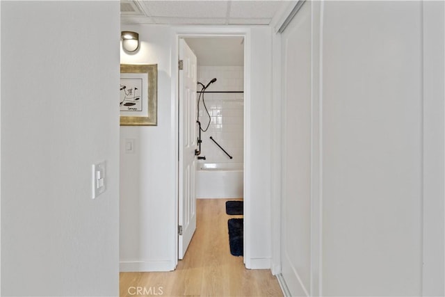 hall with a paneled ceiling and light hardwood / wood-style floors