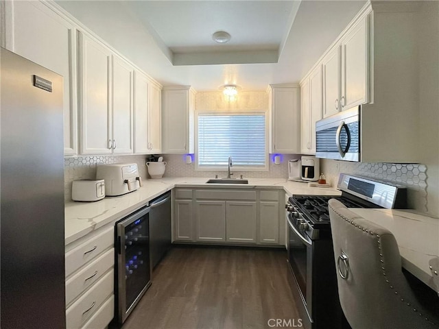 kitchen with a tray ceiling, appliances with stainless steel finishes, white cabinets, a sink, and beverage cooler