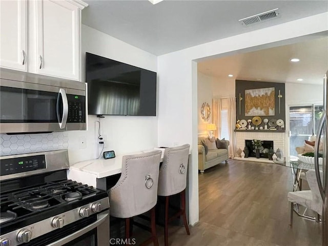 kitchen featuring visible vents, white cabinets, decorative backsplash, stainless steel appliances, and a brick fireplace