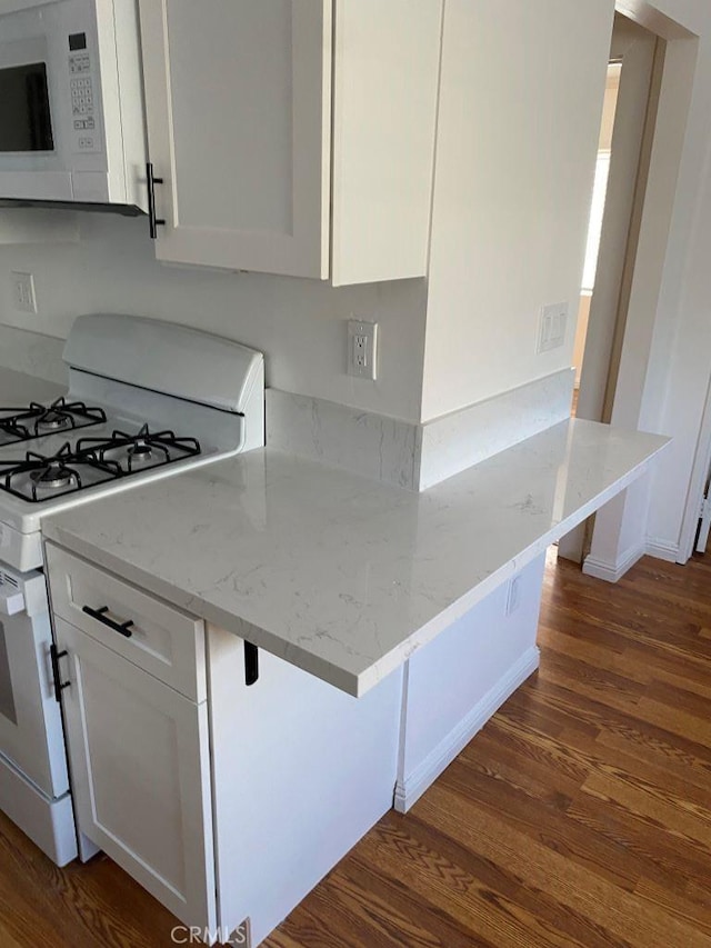 kitchen with white cabinetry, light stone counters, a breakfast bar, and white appliances