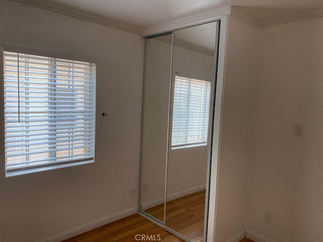 unfurnished bedroom featuring multiple windows, a closet, crown molding, and hardwood / wood-style floors