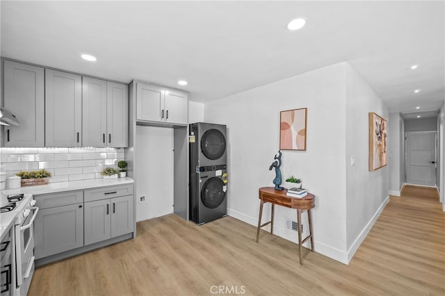 kitchen with stacked washer and dryer, gray cabinetry, backsplash, and white range with gas stovetop