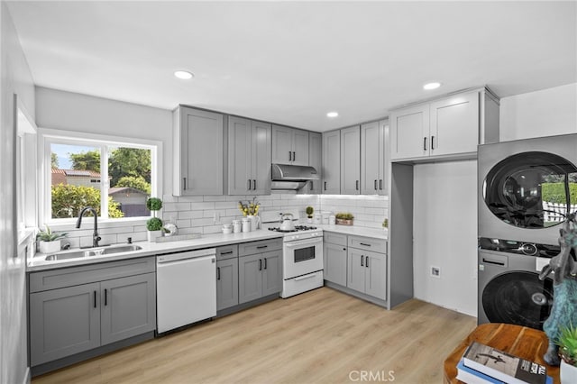 kitchen featuring stacked washer and clothes dryer, tasteful backsplash, white appliances, light wood-type flooring, and sink