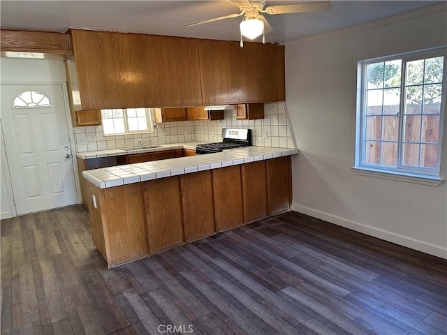 kitchen with dark wood-type flooring, backsplash, kitchen peninsula, tile countertops, and stainless steel range with gas cooktop