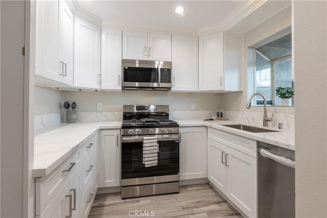 kitchen with white cabinets, stainless steel appliances, sink, light stone counters, and light hardwood / wood-style flooring