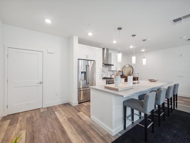 kitchen featuring wall chimney exhaust hood, high end appliances, white cabinetry, hanging light fixtures, and a kitchen breakfast bar