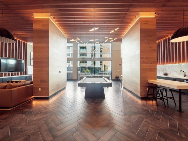 game room with sink, wooden ceiling, wooden walls, dark parquet floors, and a high ceiling