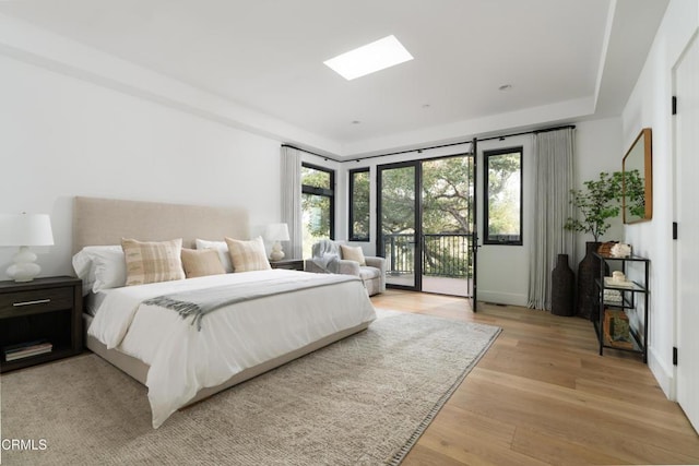 bedroom with access to exterior, a skylight, and light wood-type flooring