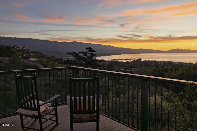 deck at dusk featuring a water and mountain view