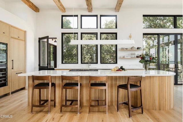 bar featuring beam ceiling, light hardwood / wood-style floors, a high ceiling, and light brown cabinets