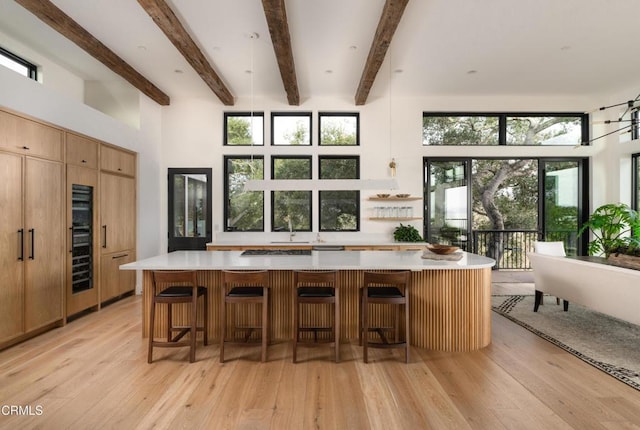 kitchen featuring beam ceiling, a breakfast bar area, light wood-type flooring, a towering ceiling, and a large island