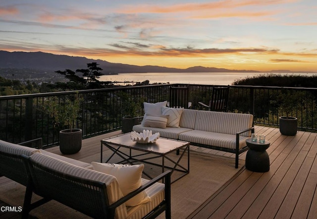 deck at dusk with an outdoor living space and a water and mountain view