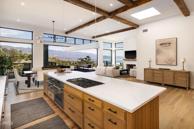 kitchen with hanging light fixtures, a center island, stainless steel gas cooktop, beamed ceiling, and light wood-type flooring