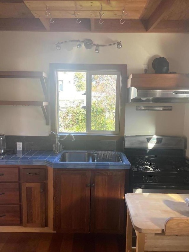 kitchen with black range with gas stovetop, tile counters, ventilation hood, and beam ceiling