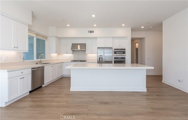 kitchen with a center island, white cabinetry, stainless steel appliances, sink, and light wood-type flooring