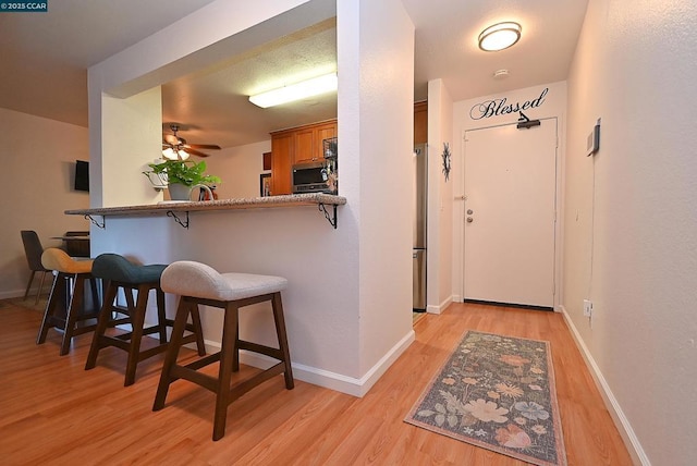 interior space with a breakfast bar, ceiling fan, kitchen peninsula, stainless steel appliances, and light hardwood / wood-style flooring