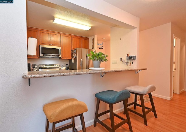 kitchen with appliances with stainless steel finishes, kitchen peninsula, a breakfast bar area, and light wood-type flooring