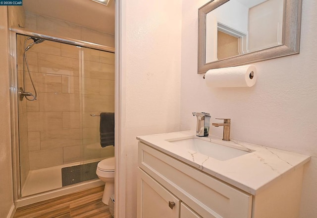 bathroom featuring hardwood / wood-style flooring, vanity, toilet, and a shower with door