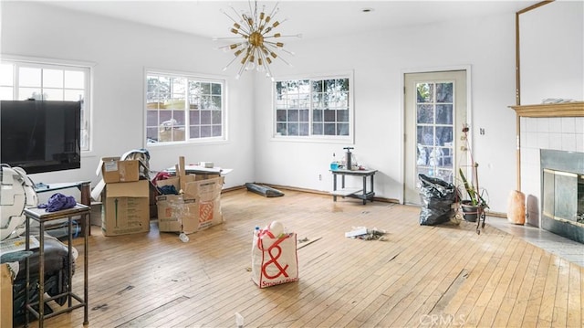 living room with wood-type flooring, a wealth of natural light, a notable chandelier, and a tiled fireplace