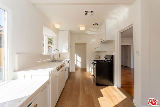 kitchen with tile countertops, black gas range, decorative backsplash, sink, and white cabinetry