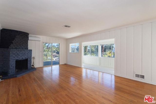 unfurnished living room with light wood-type flooring, ornamental molding, a fireplace, and an AC wall unit