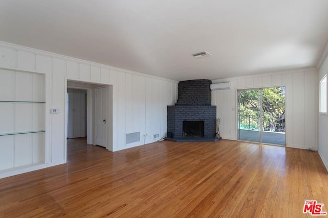 unfurnished living room with a wall mounted AC, wood-type flooring, a fireplace, and crown molding