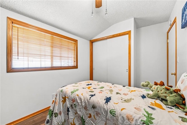 bedroom with vaulted ceiling, a textured ceiling, a closet, hardwood / wood-style flooring, and ceiling fan