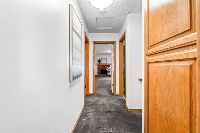 hall with a textured ceiling and dark colored carpet