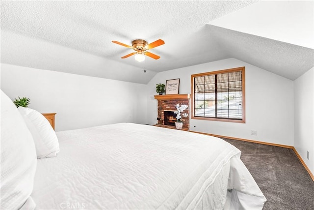 bedroom featuring vaulted ceiling, dark carpet, a textured ceiling, and a fireplace