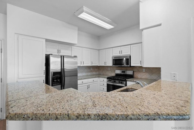 kitchen with backsplash, kitchen peninsula, sink, stainless steel appliances, and white cabinets