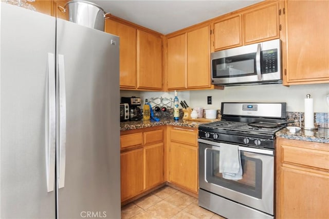 kitchen featuring stainless steel appliances, dark stone countertops, and light tile patterned flooring