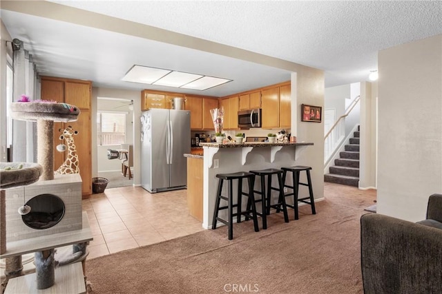 kitchen featuring kitchen peninsula, appliances with stainless steel finishes, light carpet, and a breakfast bar area