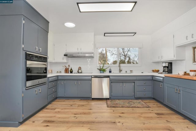 kitchen featuring tasteful backsplash, white cabinetry, sink, stainless steel appliances, and light wood-type flooring