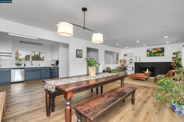 dining room featuring sink, built in shelves, light hardwood / wood-style flooring, and a brick fireplace