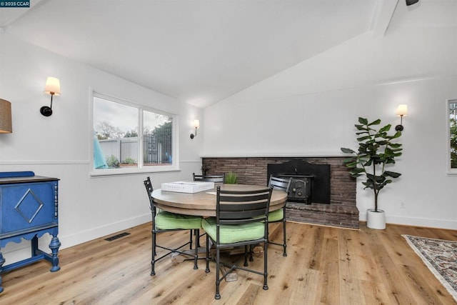 dining space featuring vaulted ceiling with beams, light hardwood / wood-style floors, and a wood stove