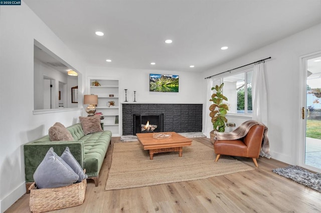 living room featuring a brick fireplace, built in shelves, and light hardwood / wood-style flooring