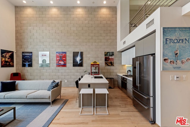 kitchen featuring white cabinetry, a kitchen bar, stainless steel appliances, a kitchen island with sink, and light hardwood / wood-style flooring