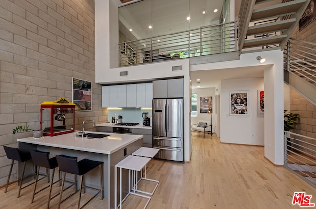 kitchen featuring a high ceiling, stainless steel appliances, sink, a breakfast bar, and light hardwood / wood-style flooring