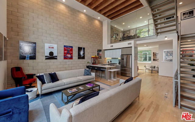 living room with light hardwood / wood-style floors, a towering ceiling, and beamed ceiling