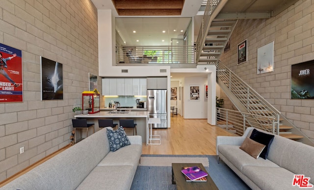 living room with sink, brick wall, light hardwood / wood-style flooring, and a towering ceiling