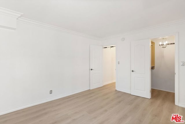 unfurnished bedroom with an inviting chandelier, a walk in closet, ornamental molding, and light wood-type flooring