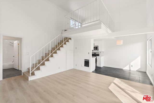 unfurnished living room featuring wood-type flooring, heating unit, ornamental molding, and a towering ceiling