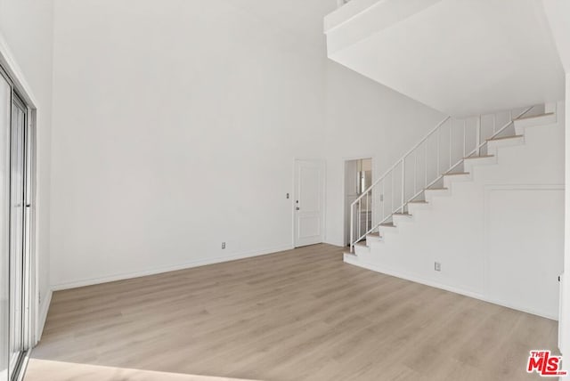 unfurnished living room featuring light wood-type flooring and a high ceiling