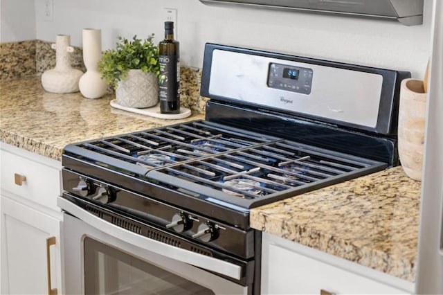 details featuring gas range, light stone countertops, and white cabinets